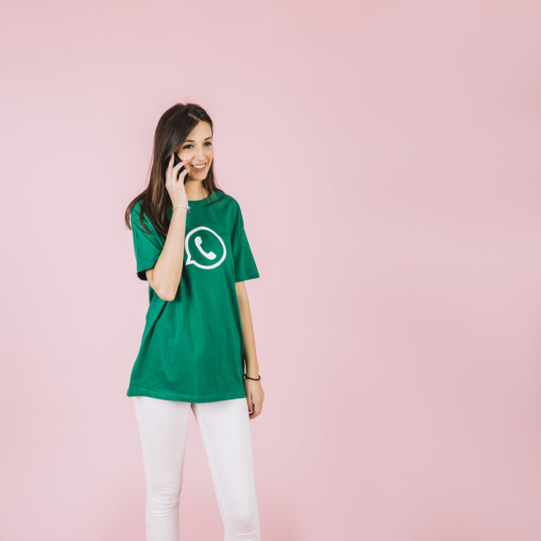 smiling young woman talking smartphone against pink backdrop